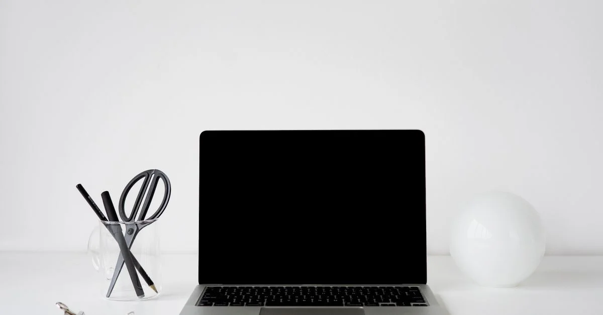 Bureau moderne et minimaliste avec un ordinateur portable, des stylos et des éléments décoratifs blancs sur un bureau blanc.